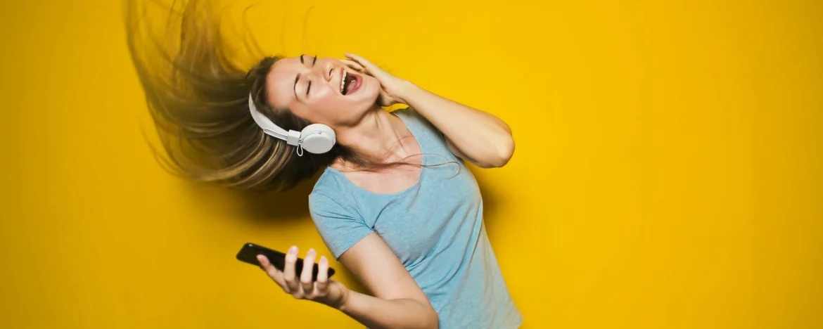 Woman enjoying listening to music on headphones with yellow background.