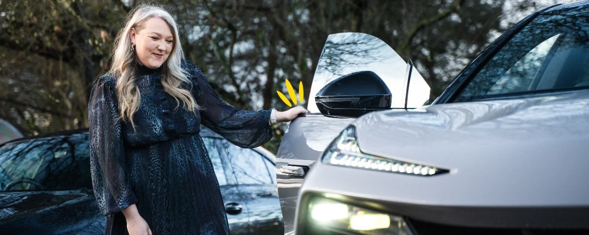 Woman in dress standing next to car smiling