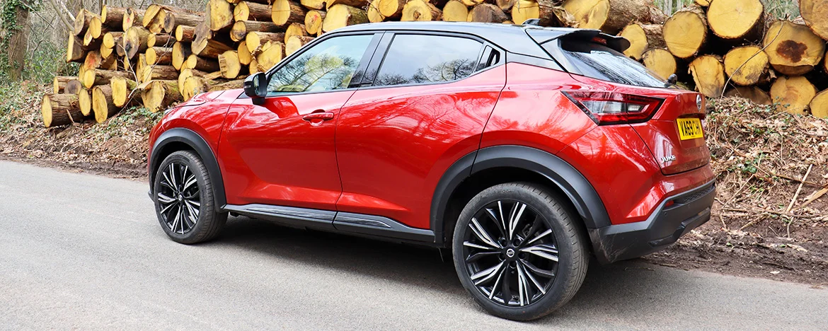 Red Nissan Juke parked in front of timber stacks