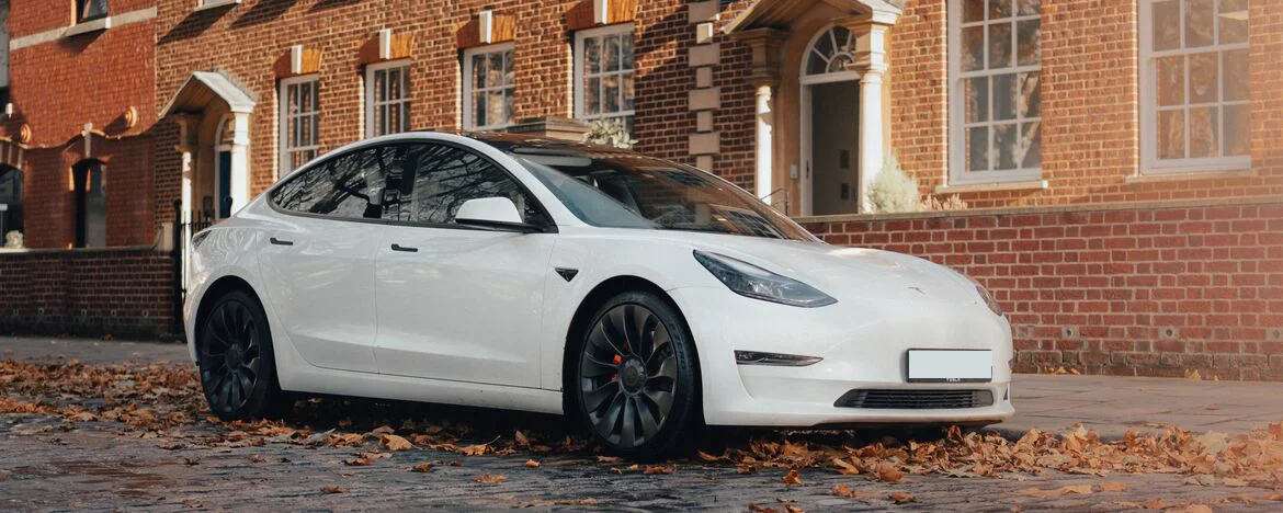 A white Tesla parked outside a posh brick building. 