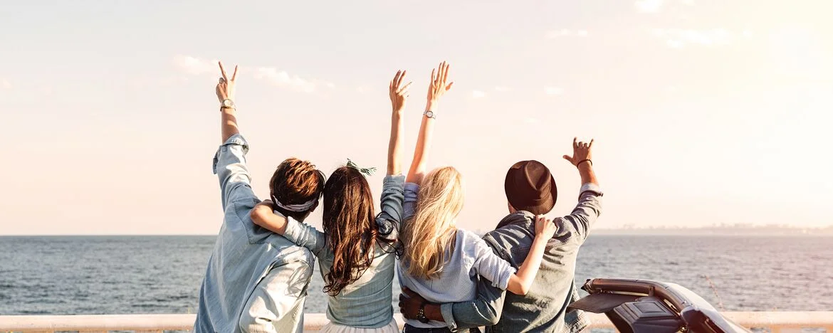 Four friends sat on their car looking out over a sea view