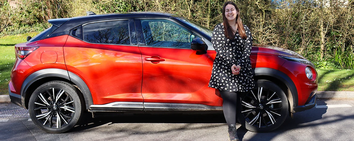 Smiling woman stood next to red Nissan Juke Tekna