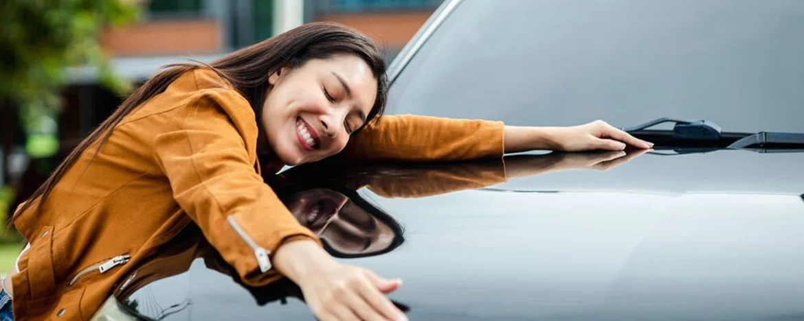 Woman hugging her car bonnet while smiling