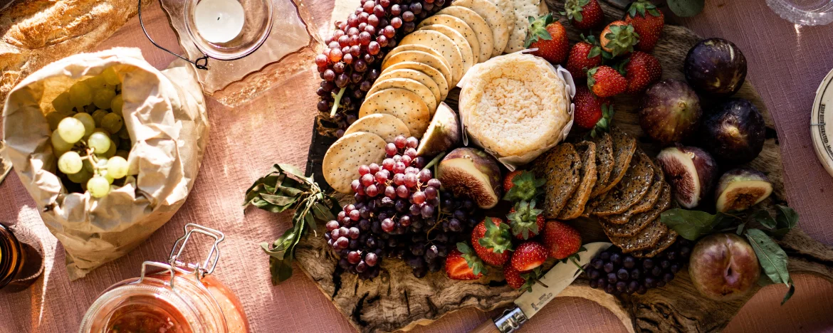 Close up of a picnic blanket with crackers, fruit and chutney