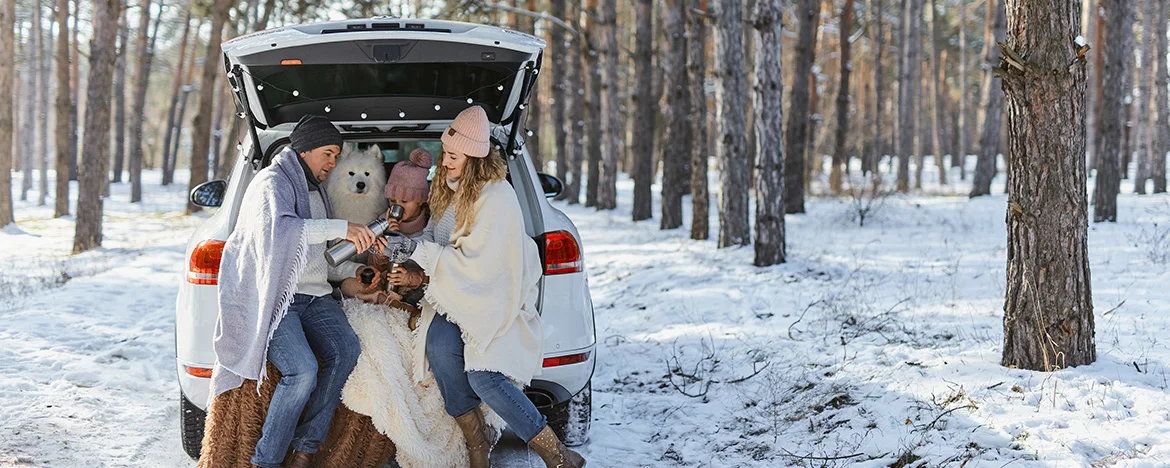 Happy family and dog sat in the boot of their car in a snowy forest