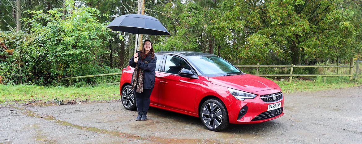 Woman with umbrella standing next to Corsa-e