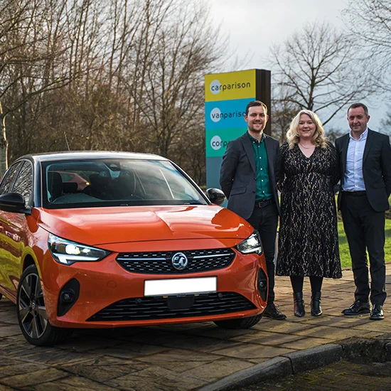 Carparison GM and two senior managers standing next to Orange Vauxhall Corsa Electric