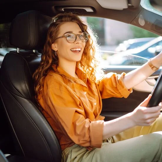 Smiling woman in orange shirt driving a car