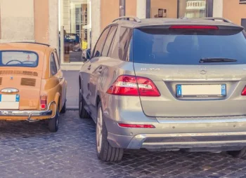 A small retro car parked next to a modern day SUV
