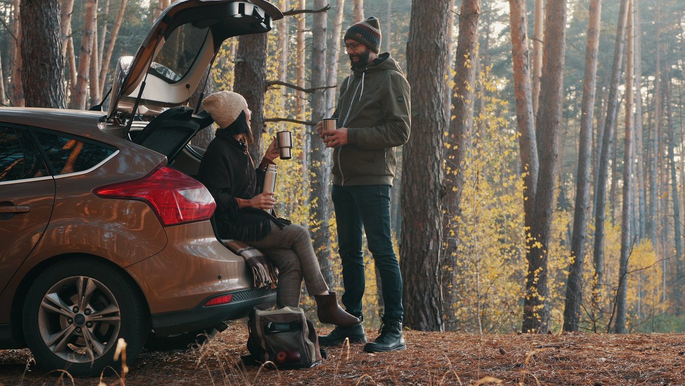 A man and women sat drinking a hot drink out of car boot