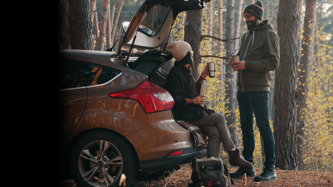 A man and women sat drinking a hot drink out of car boot
